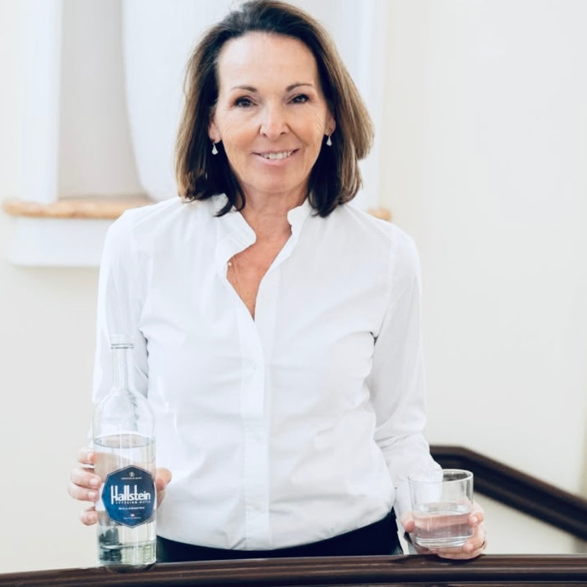 Woman holding a bottle and glass of Hallstein water 